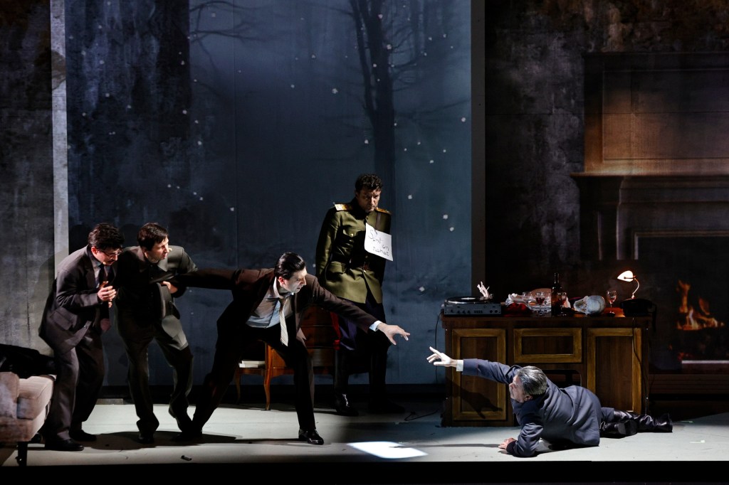 A dramatic scene depicting five men in suits and a soldier in uniform surrounded by an office setting, with one man reaching out from the floor while others stand in various poses of tension.