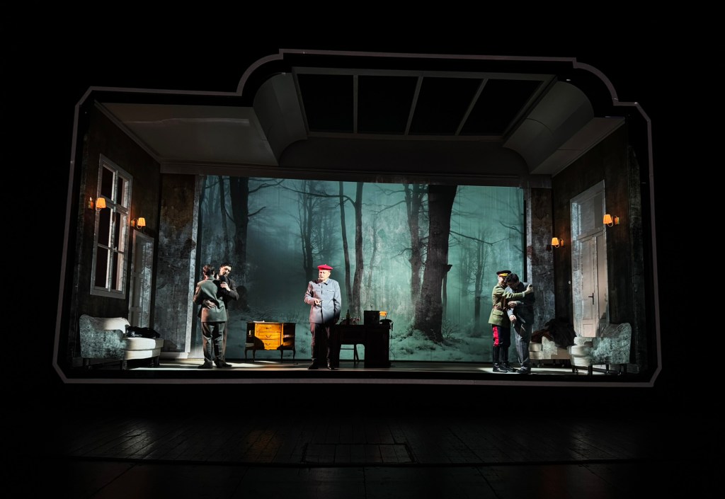 A theatrical scene set in a dimly lit room with actors performing against a backdrop of a foggy forest.